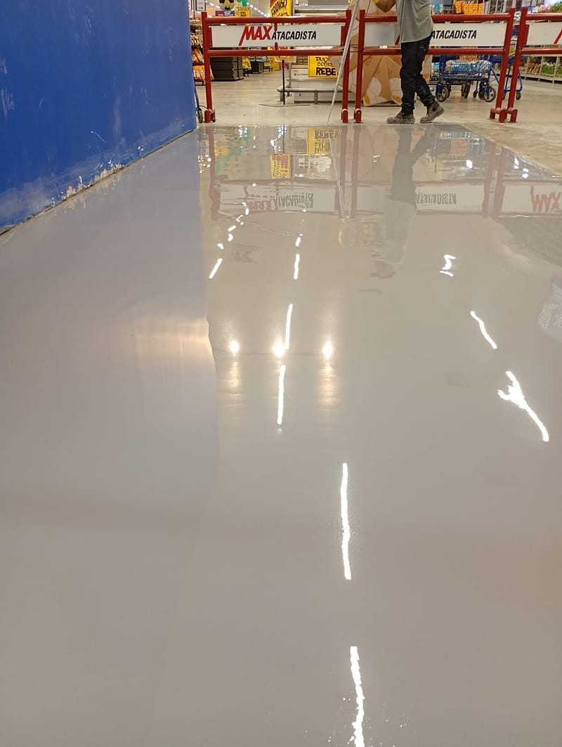 Revestimento de uretano cinza brilhante em loja do Max Atacadista de Interlagos, refletindo as luminárias, com as cancelas da loja ao fundo